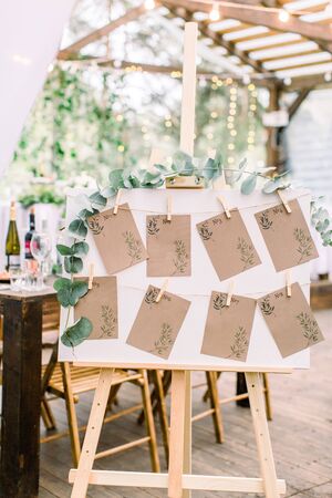 Decorated seating plan for wedding guests in woodent tent restaurant outdoors. Original rustic wooden board with guest listの写真素材