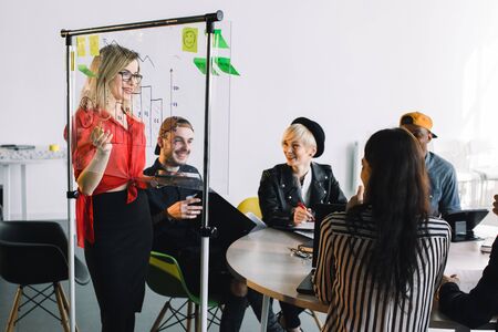 Portrait of young female team leader of talented freelances organizing work of members motivates and inspire them to make researching, standing near glass board in modern coworking spaceの写真素材