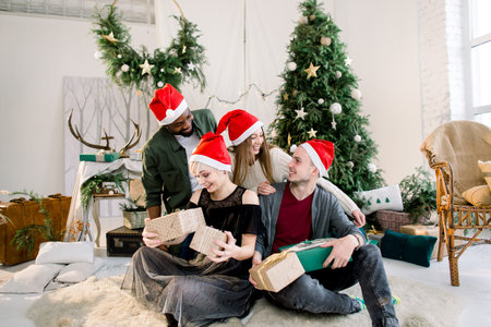 Cheerful young four international people celebrate Christmas and New Year together in cozy decorated...