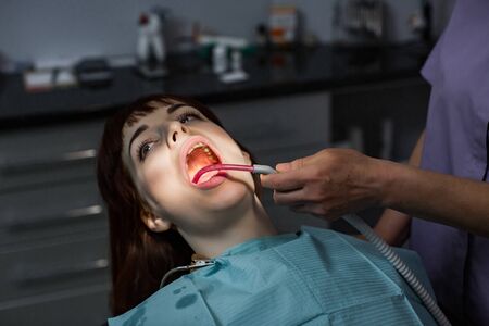 Young woman patient having dental treatment at dentists office. Dentist assistant holding salive ejectorの写真素材