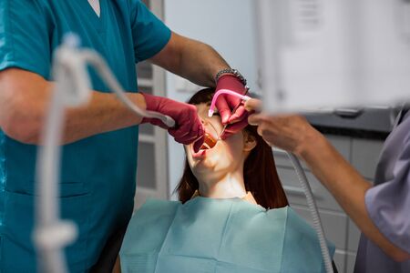 Young woman patient in dental clinic having dental check and treatment, woman with open mouth, professional dentist teamの写真素材