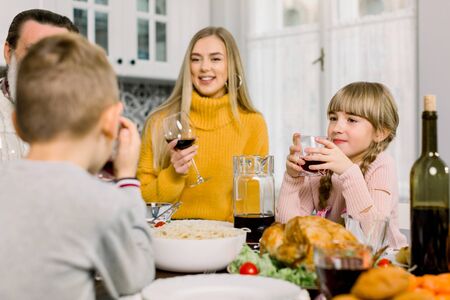 happy young mother and cute little daughter holding glasses with drinks at thanksgiving holiday table. Family dinner, mother with children boy and girl, grandfather at the tableの写真素材