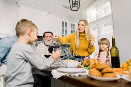 Pretty young mother pouring cherry juice for son at holiday dinner. happy large family having holiday dinner on thanksgiving dayの写真素材