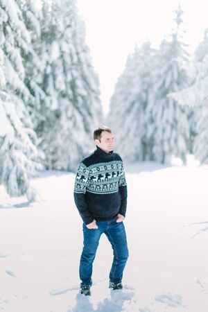 Handsome young man in knitted sweater poses on the snow in cold winter forest. Winter holidays, Christmas, New Year concept. Love in winter.の写真素材