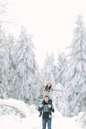 Happy young lovely Couple in winter knitted sweaters walking in snowy forest piggyback.の写真素材