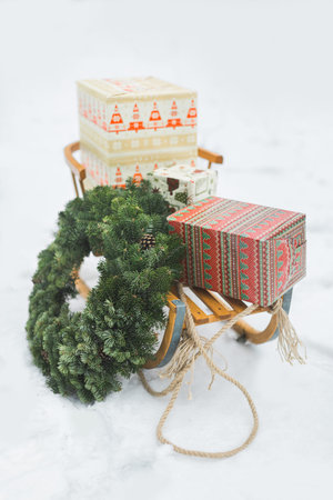 Christmas wreath and presents boxes on wooden sledge on white frosty snow background, winter time...