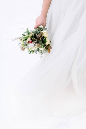 Wedding bouquet with flowers and cotton in hands of the bride. Winter time, snowy forest. Cropped image.の写真素材