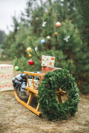 Beatiful wooden Santa's sledge with Christmas gifts and wreath, over the background of winter forest and decorated Christmas tree. Merry Christmas and Happy New Year Conceptの写真素材