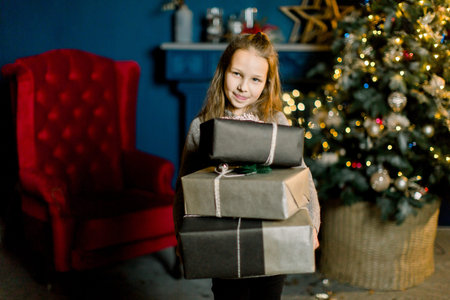 Little beautiful girl holds christmas gifts and happy from thisの写真素材