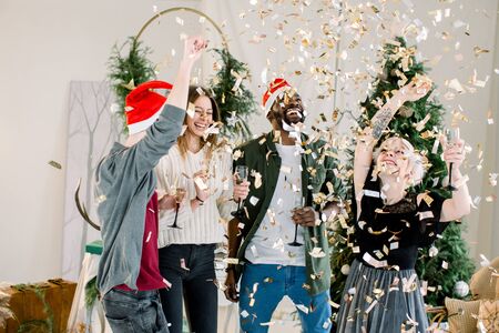 Group of four cheerful fashion dressed friends standing in front of Christmas decorations and celebrating New Year, drinking champagne.の写真素材