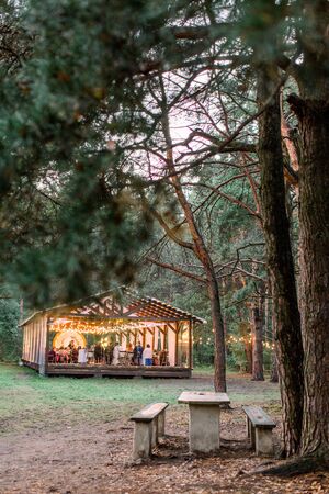 Stylish rustic restaurant wooden tent with wooden tables and chairs. Vintage design of the restaurant in the forest, decorated with lamps light bulbs. Wedding rustic outdoors.の写真素材
