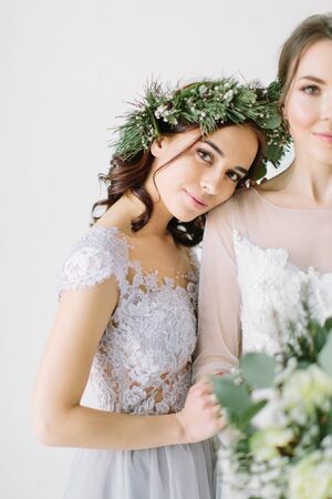 Bridesmaid in pine wreath and blue dress holding her hand on the arm of bride in white wedding dress standingの写真素材
