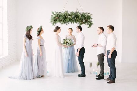 Young fashionable lovely couple together with bridesmaids and groommen with speech master of wedding ceremony against decor pine arch on wedding anniversary and marriage proposal.