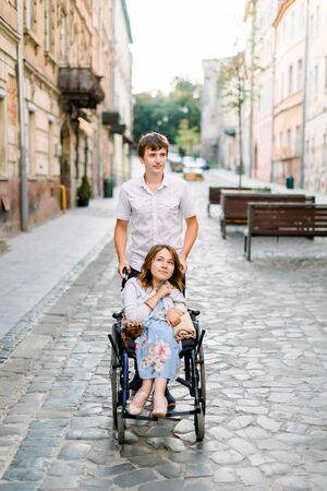 Young Couple In Wheelchair Strolling In The City. Pretty young woman in wheelchair and her boyfriend in the center of old cityの写真素材