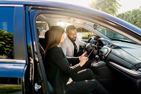 Young African American man communicating with female Caucasian coworker during car drive to business meeting discussing startup ideas and presentation from digital tabletの写真素材