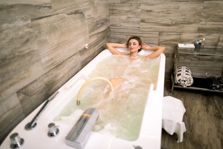 Happy Caucasian young woman relaxing in the hydro massage bath, holding hands behind headの写真素材