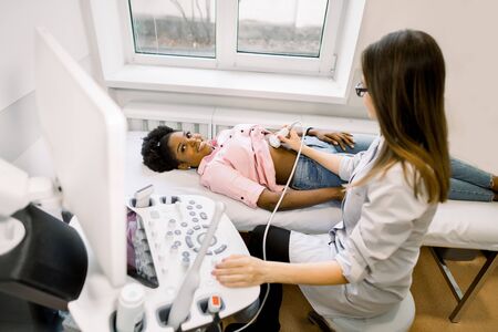 Ultrasound diagnostic of stomach on abdominal to young African woman. Doctor runs ultrasound sensor over patient's tummy and working on scanner panel. Diagnosis of internal organsの写真素材