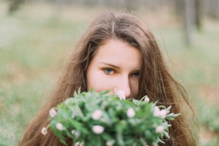 beautiful woman with flowers walking through the green forest in early springの写真素材