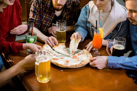 Multiracial happy young people eating pizza in pizzeria, cheerful friends laughing enjoying meal having fun sitting together at restaurant table, diverse friends share lunch at meetingの写真素材