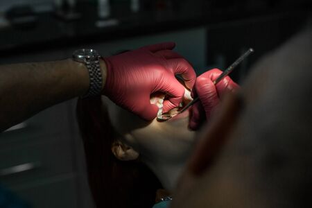 Cropped image of hands of senior man doctor dentist doing treatment and dental care for his young female patientの写真素材