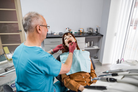 Senior male dentist with young female patient during oral checkup in modern dentistry clinic.