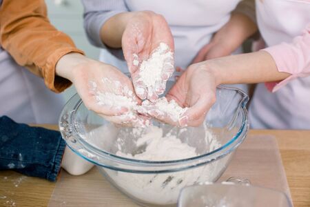 Grandma and her daughters keep flour in their hands, prepare a dough in their kitchenの写真素材