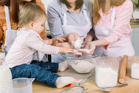 Little beautiful baby girl with mother, aunt and grandmother holding flour in their hands and making...