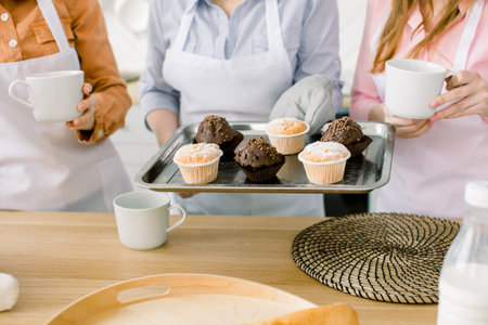 Cupcake, muffins, baking together - three women hold freshly baked chocolate and vanilla cupcakes on...