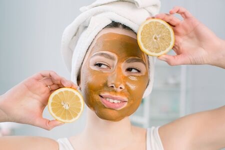 Funny beautiful model holding lemon slices up to her eyes. Photo of girl with moisturizing brown facial mask. Beauty and Skin care concept.の写真素材