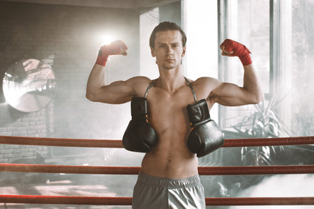 Portrait of muscular handsome boxer relaxing on boxing ring background.