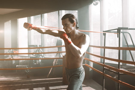 Young handsome boxer pulls training punching with rubber band in boxing ring