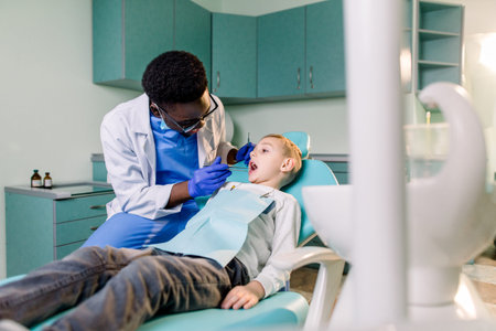 Young beautiful boy in dental office. Children's African-American dentist examines teeth to a childの写真素材