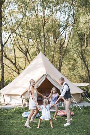 Family, leisure, holidays and people concept. Happy beautiful family with children dancing and having fun at summer in garden, boho wigwam tent on the backgroundの写真素材