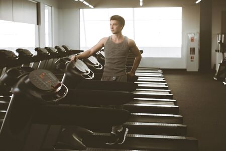 Portrait of a fit man in sportswear standing beside a treadmills in a gym. Active Lifestyle. Getting Better. Gym Equipment.の写真素材