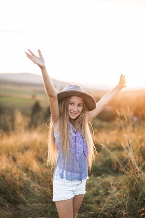 Little blond girl posing in a wild summer field with her arms holding up and a smile on her face. Summer walk, child in fieldの写真素材