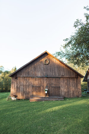 Stylish wooden barn in countryside, on green grass. Summer sunset. Wooden barn in rural area, summer...
