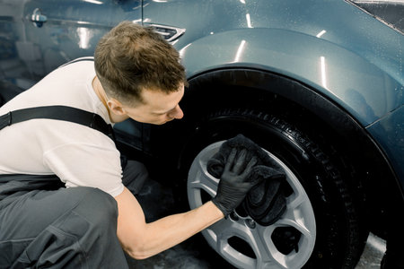 Side view of handsome Caucasian male car wash worker hodling in hand black microfiber cloth and...