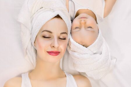 Top view of beautiful young mother and her two year old daughter lying on the bed at home, relaxing after nice spa bath procedures with eyes closed. Family spa and beauty careの写真素材