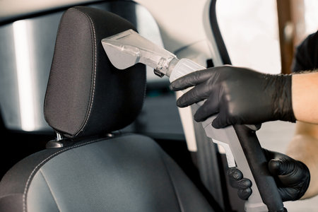 Cropped image of hands of car service worker, wearing black protective gloves, cleaning car front...