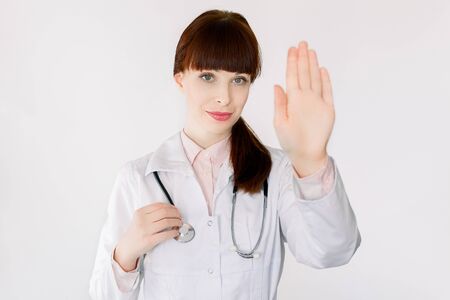 Young female GP doctor gesturing stop Coronavirus disease, COVID-19, 2019-ncov, global pandemic outbreak, standing over white background. Not spread virus worldwide, stay safe at home conceptの写真素材