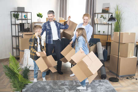 Cheerful Caucasian family holding and playing with boxes while standing at bright modern apartment. Happy family moving to new house. Concept of property and real estate.の写真素材