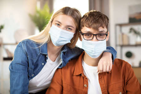 Students, man and woman in casual outfit and face masks posing on camera, sitting at the table and using laptop. Young partners cooperating or working remotely online from homeの写真素材