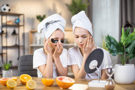 Two caucasian teen sisters with towel on had taking care of soft skin under eyes using collagen patches. Concept of youth, beauty routine and healthy lifestyles.の写真素材
