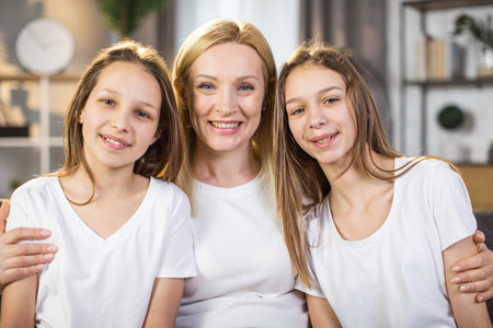 Portrait of attractive middle aged woman embracing her two pretty daughters while sitting at table...