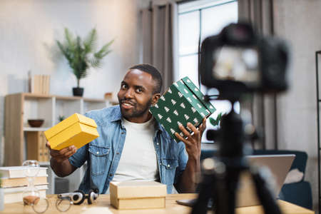 Positive african american man doing live stream while opening presents at home. Male influencer creating new content for his social networks.の写真素材