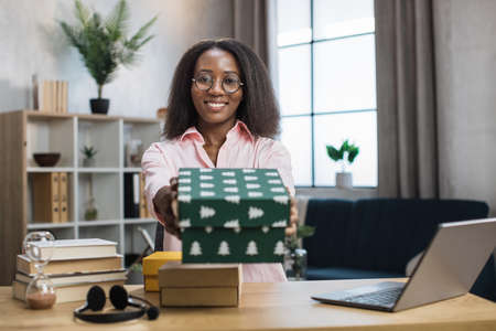 First person view of african female blogger opening gift boxes while sitting at home. Positive young woman doing live stream during unpacking process.の写真素材