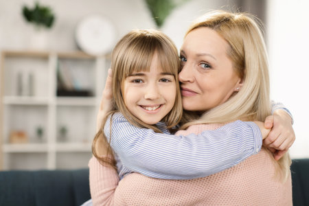 Mother and daughter sitting together on sofa at home embracing feels happy and satisfied. Beautiful...