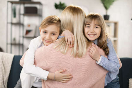 Happy affectionate family mom and two cute little kids embrace and looking at the camera, smiling foster parent mother and small girl and boy hugging cuddling enjoy tender warm moment, close up viewの写真素材