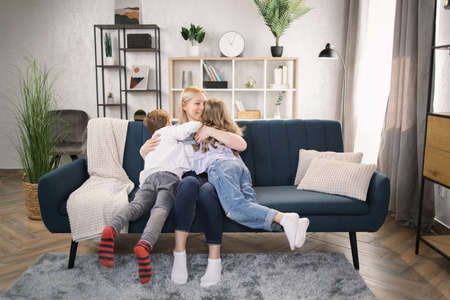 Close up portrait of excited young mother and little preschooler children hug cuddle look at camera laughing and posing together, overjoyed mom or nanny relax play with small kids at homeの写真素材
