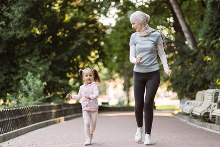 Family sports and outdoor activity concept. Cheerful young Muslim Arabian woman enjoying running together in park with her cute active 4-aged daughter. Mom and child jogging in the parkの写真素材